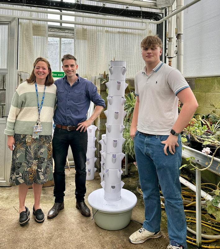 Staff and a student beside a Harvestory growing tower delivered to a college greenhouse