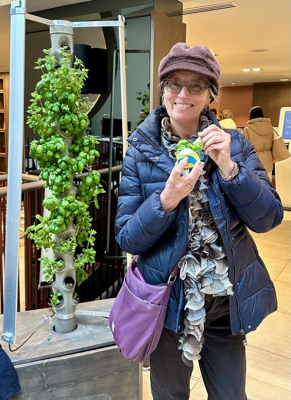 A person holding a freshly made drink beside a Harvestory growing tower
